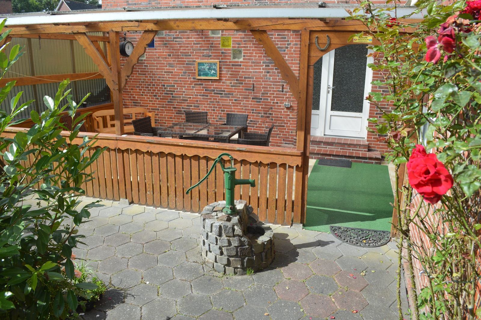 Terrasse des Ferienhauses in Rysum mit alter Wasserpumpe und Garten